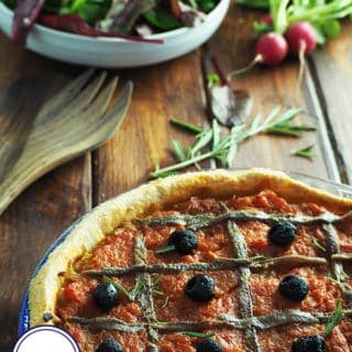 A rustic onion and tomato tart on a table with a bowl of salad