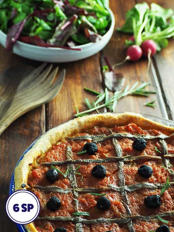 A rustic onion and tomato tart on a table with a bowl of salad