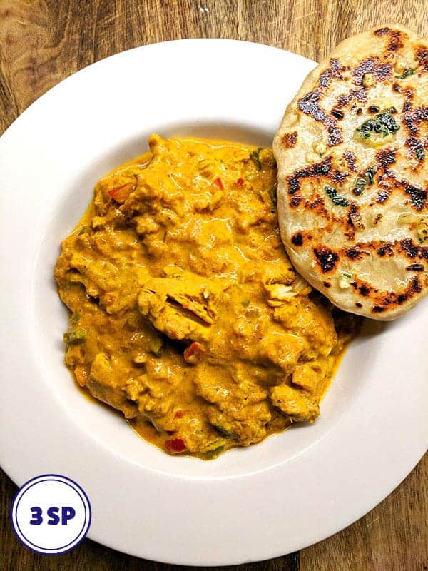 A white bowl of chicken tikka masala with a garlic naan