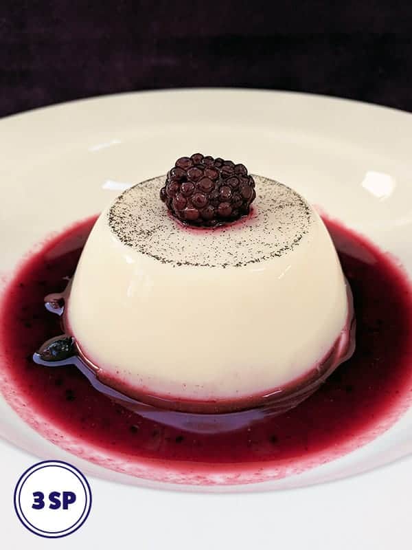 A milk jelly with a blackberry on top and surrounded by berry coulis