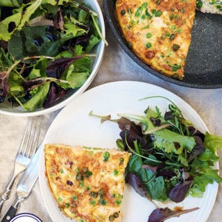 A top down photograph of a salmon frittata on a white plate with salad