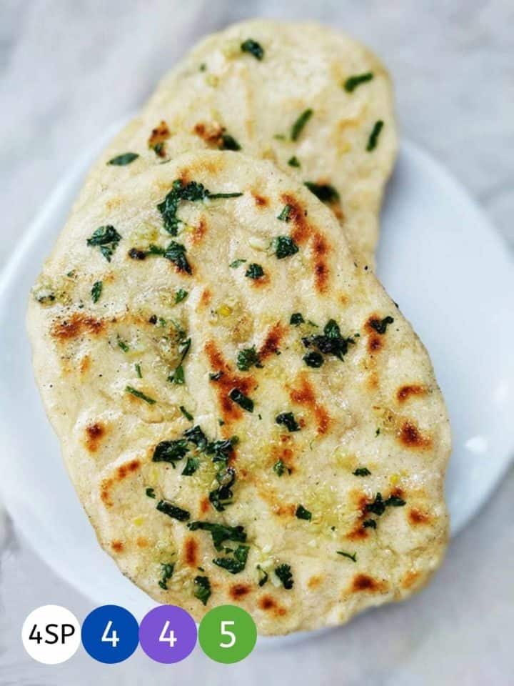 2 garlic naan breads on a white plate on a white marble table.