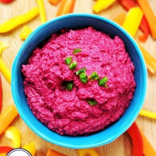 A bright pink beetroot hummus in a blue bowl surrounded by chopped peppers