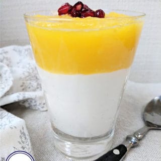 A glass of parfait topped with mango and pomegranate