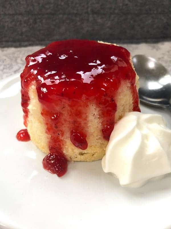 A raspberry jam sponge cake topped with raspberry jam on a white plate.