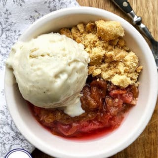 A white bowl with rhubarb , crunchy biscuit and ice cream