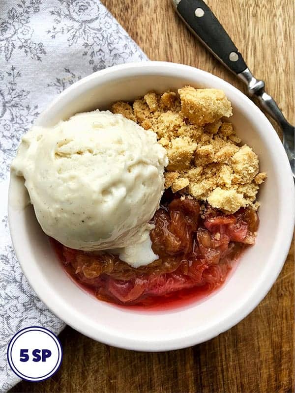 A white bowl with rhubarb , crunchy biscuit and ice cream