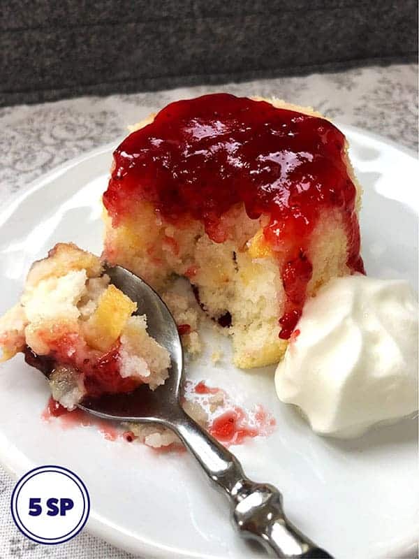 A pear sponge topped with raspberry jam on a white plate