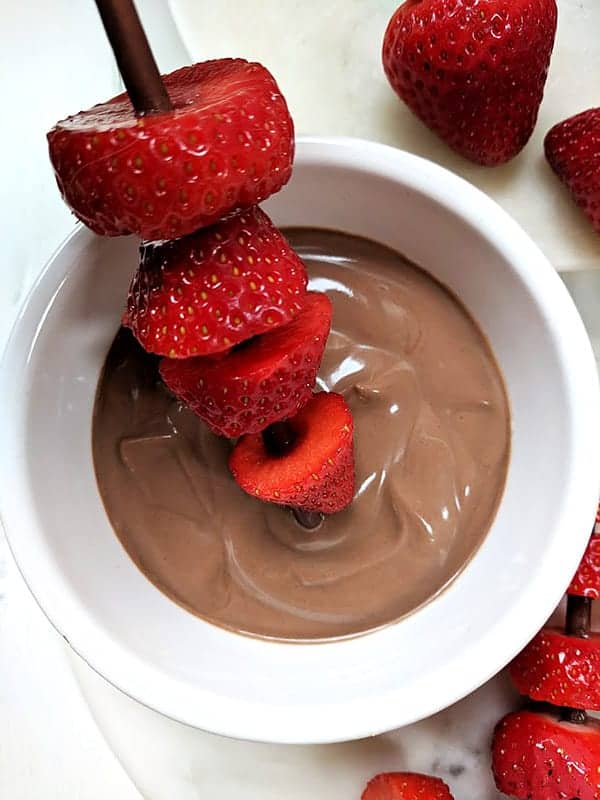 A strawberry kebab being dipped into chocolate dipping sauce