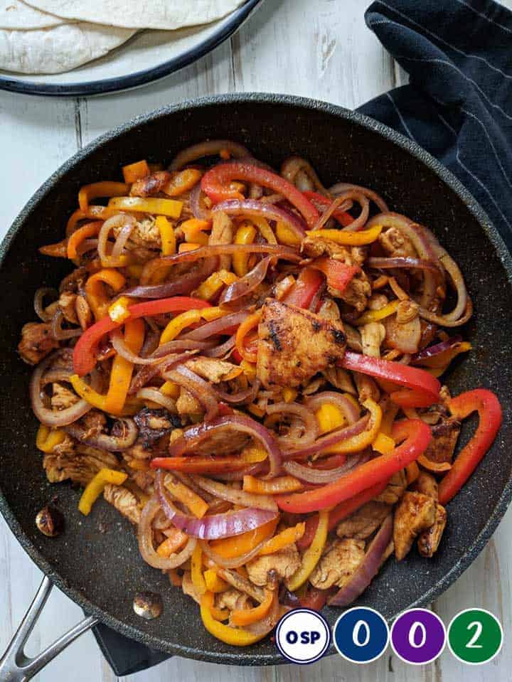 A skillet of chicken fajitas on a white table