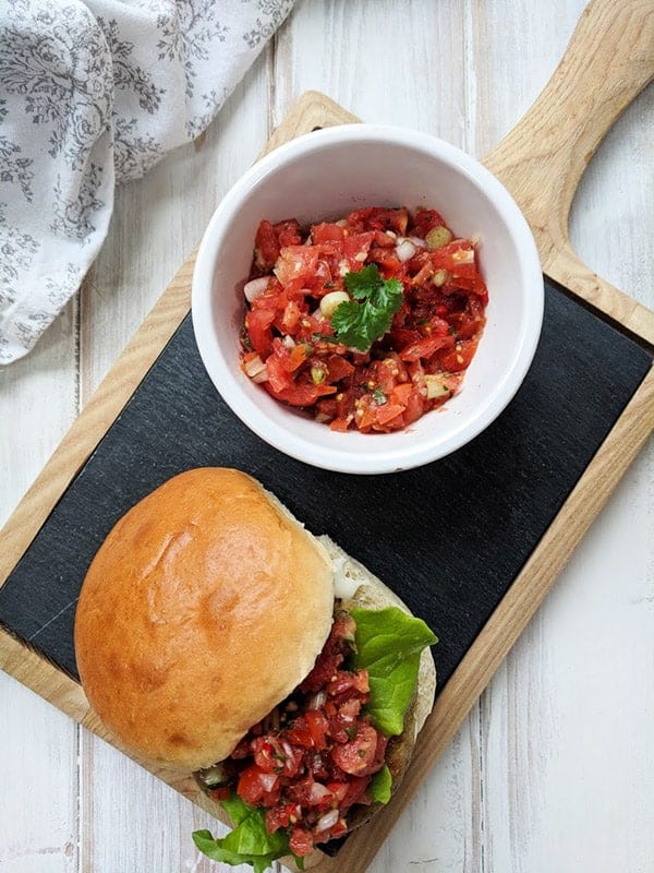 A Falafel burger on a board with a dish of salsa