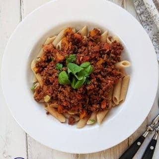A white bowl of pasta topped with Bolognese sauce
