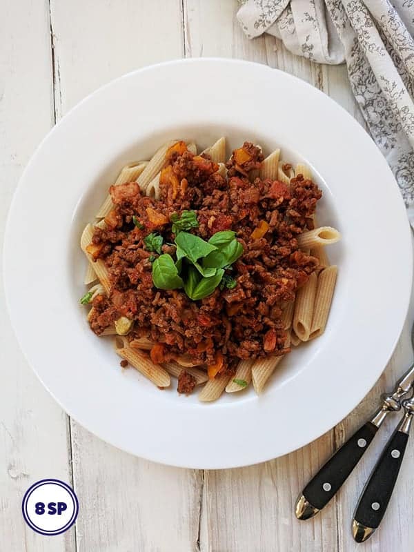 A white bowl of pasta topped with Bolognese sauce 