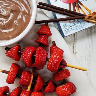 Some strawberry kebabs next to a box of mikado sticks