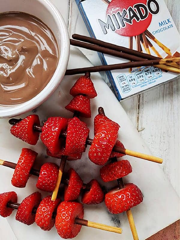 Some strawberry kebabs next to a box of mikado sticks