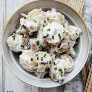 A white bowl of potato salad topped with chopped chives