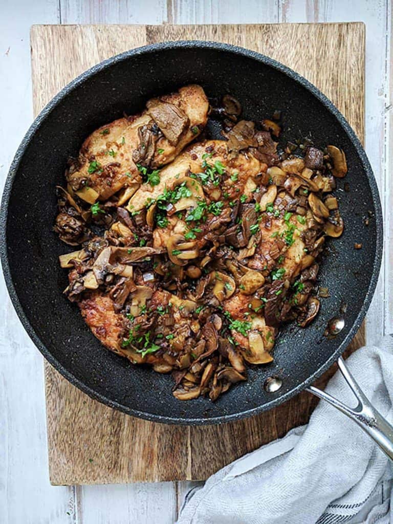 A skillet of chicken marsala on a wooden board