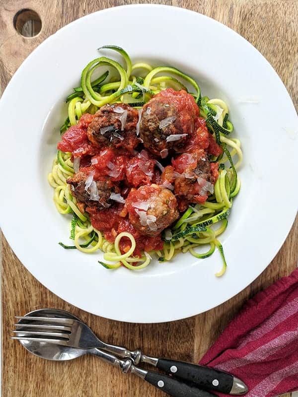A white bowl full of zuchinni noodles and italian meatballs