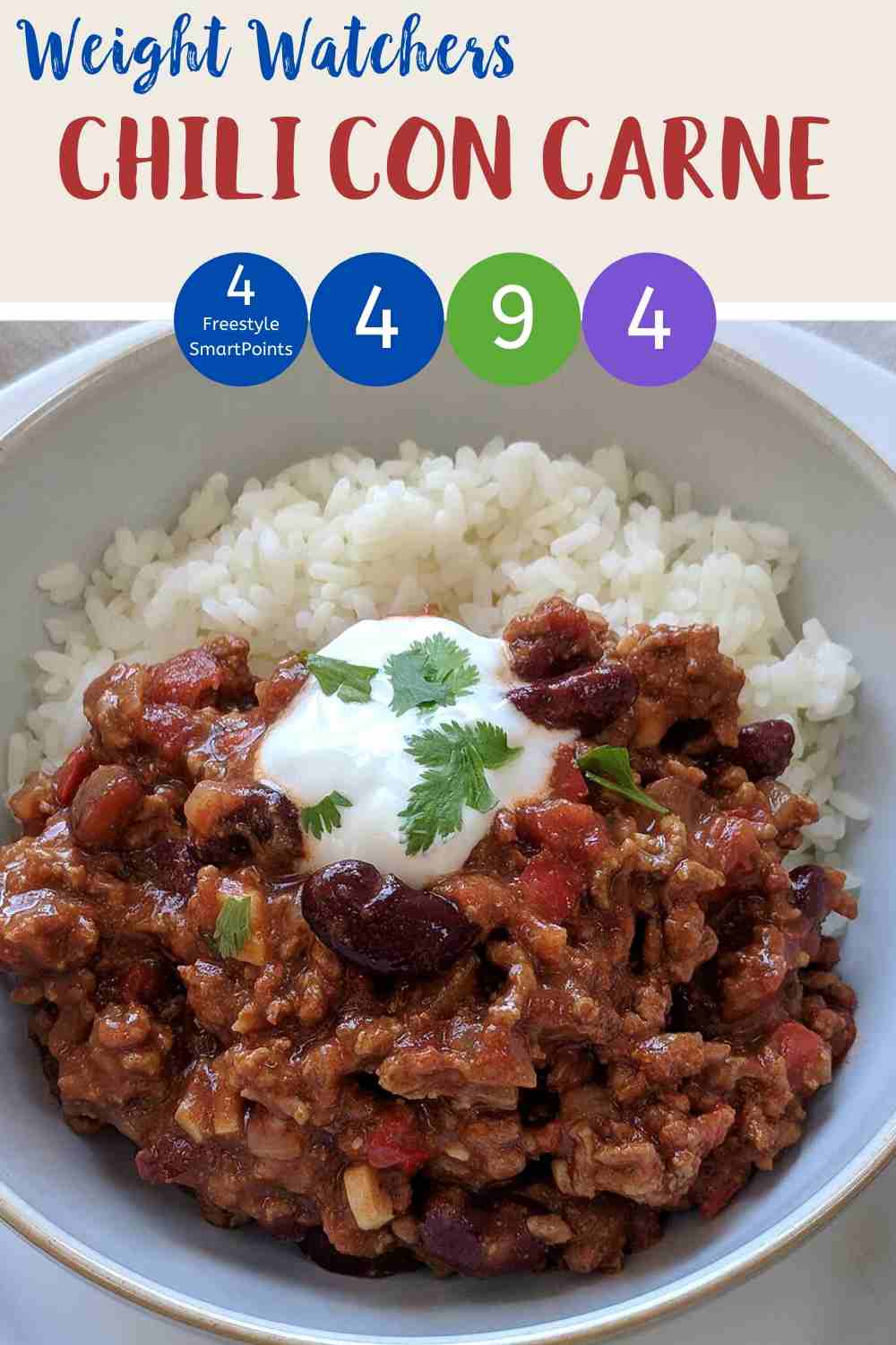 A white bowl filled with chili con carne & rice topped with yogurt and green herbs