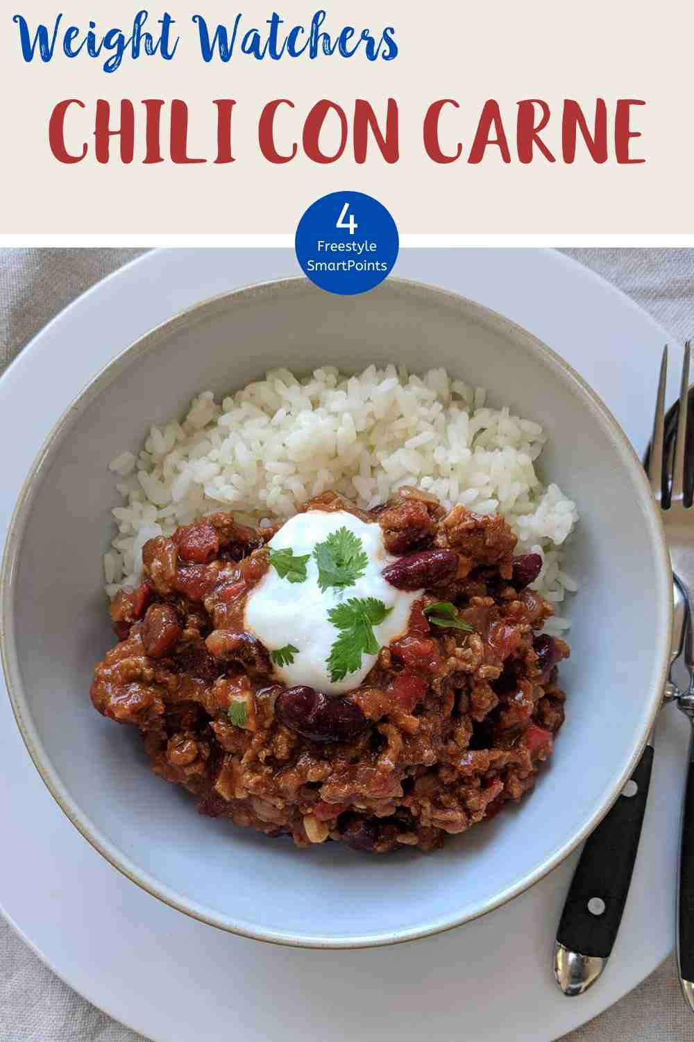 A white bowl filled with chili con carne & rice topped with yogurt and green herbs