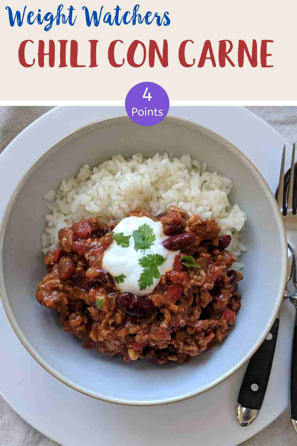 A white bowl filled with chili con carne & rice topped with yogurt and green herbs