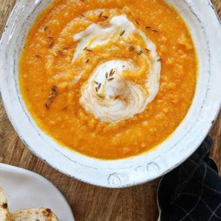 A bowl of carrot & lentil soup on a wooden board