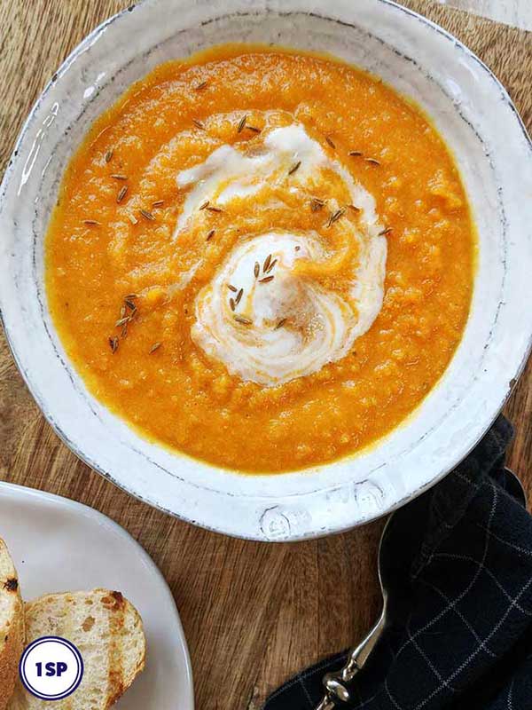 A bowl of carrot and lentil soup on a wooden board