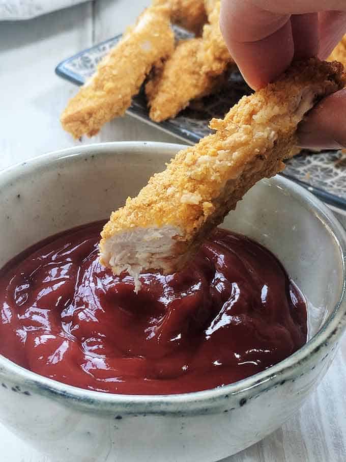 A chicken tender being dipped into tomato sauce