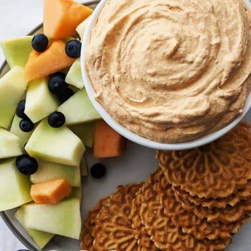 A white bowl of pumpkin fluff surrounded with fruits and cookies