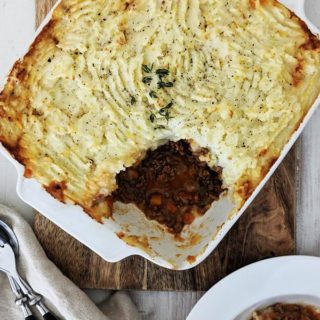 A white dish of cottage pie on a wooden board