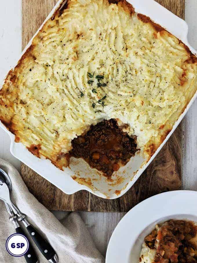 A white dish of cottage pie on a wooden board