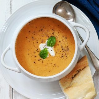 A white bowl of creamy tomato soup with some bread.