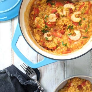 A pot of shrimp, chorizo and red pepper paella on a white table