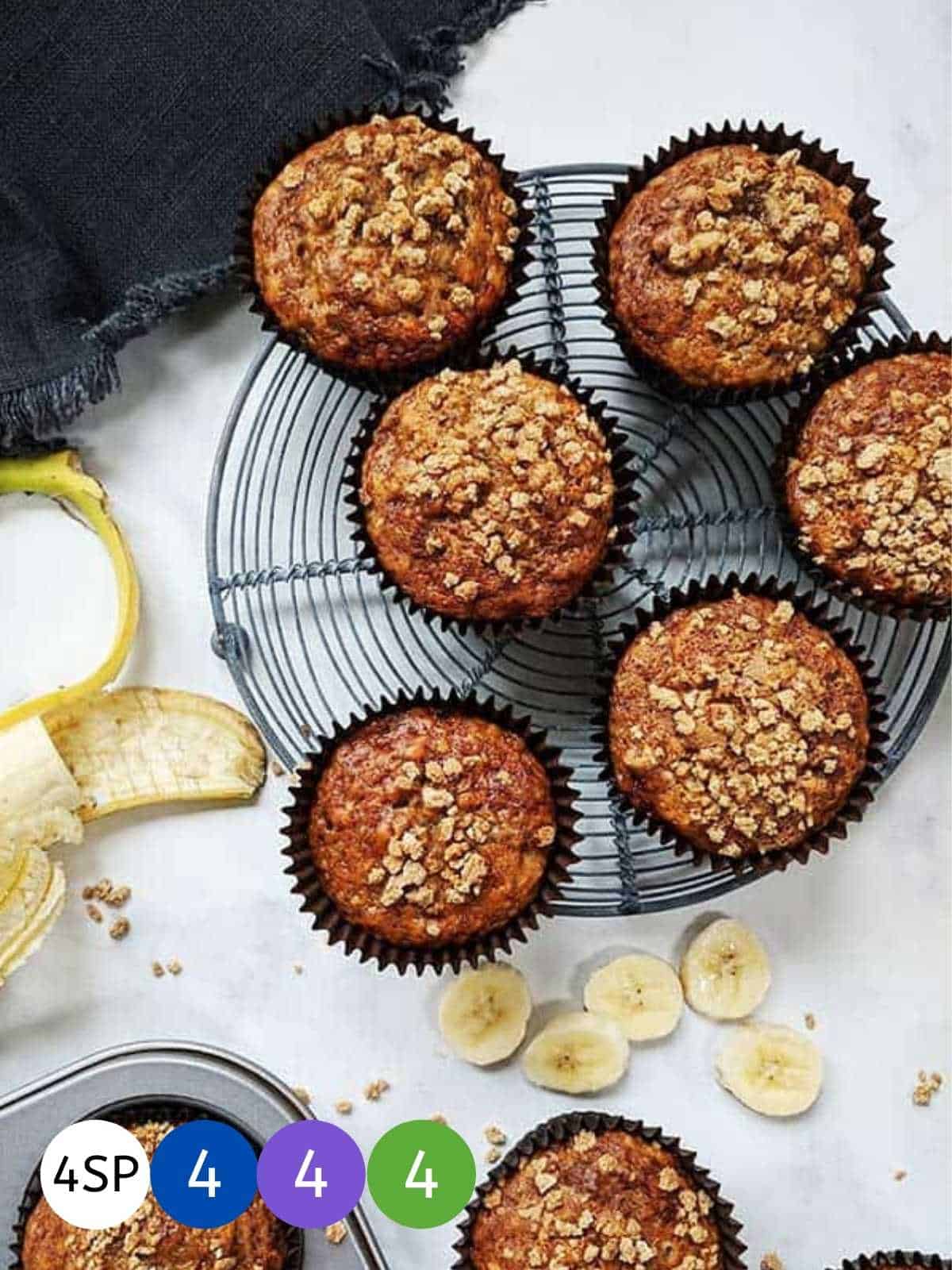 Six banana muffins on a wire rack cooling with banana slices beside them.