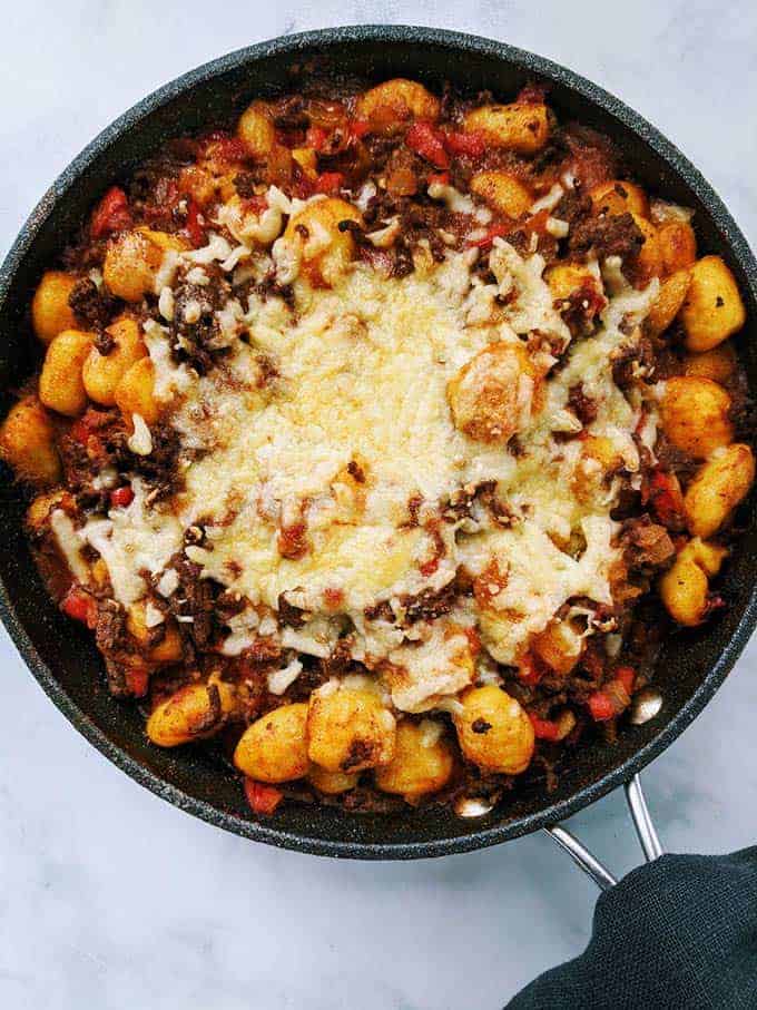 A skillet of spicy ragu gnocchi with melted cheese