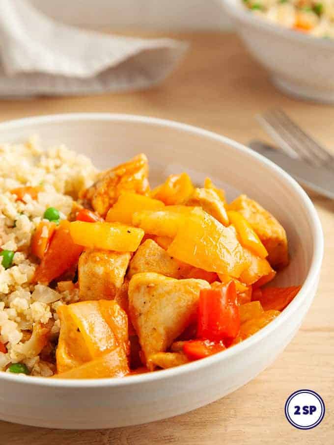 A white bowl full of sweet and sour chicken with egg fried rice