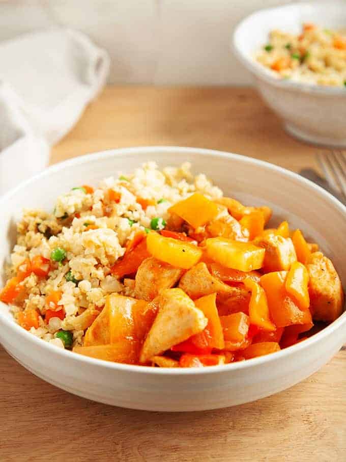 A bowl of sweet and sour chicken in a white bowl on a wooden table