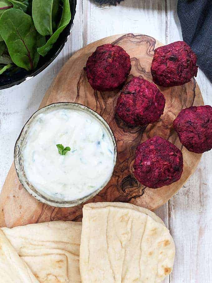 Five beetroot falafels on a board with some tzatziki and flatbreads