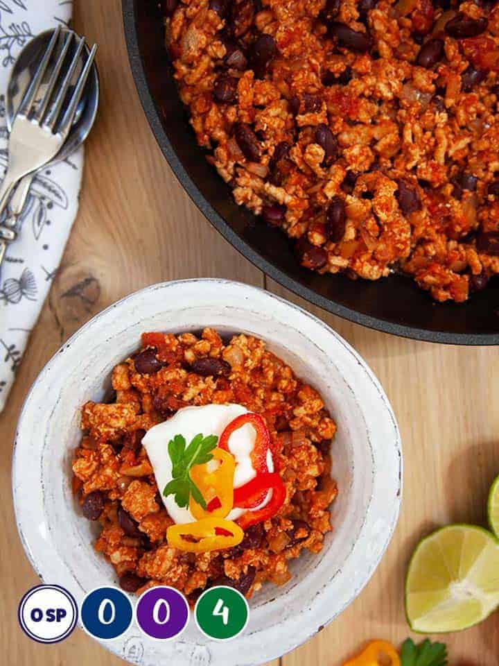 A wooden table with a skillet and bowl of chili