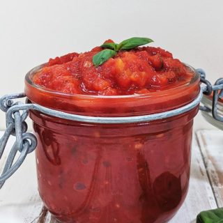A jar of easy marinara sauce on a white table with basil leaves