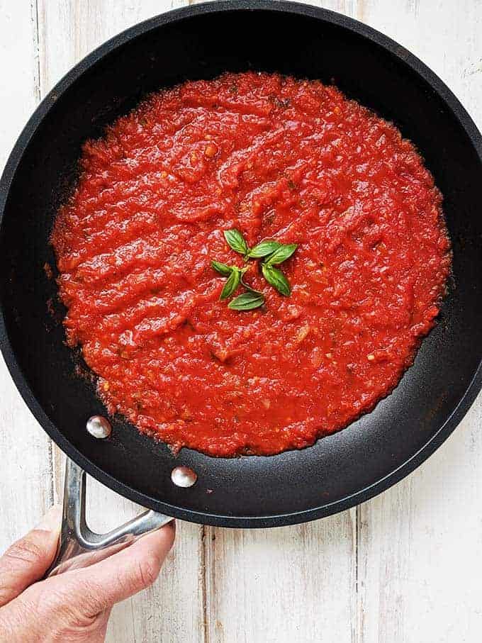 Bright red marinara sauce in a black skillet on a white background