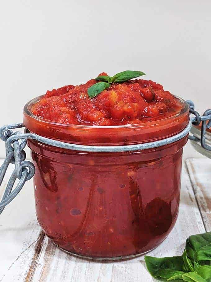 A jar of easy marinara sauce on a white table with basil leaves