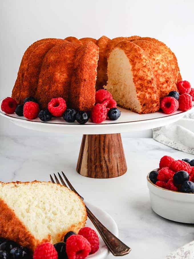 A pineapple angel food cake on a cake stand surrounded by berries