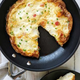 A skillet of sweet pepper frittata with mozzarella on a white table