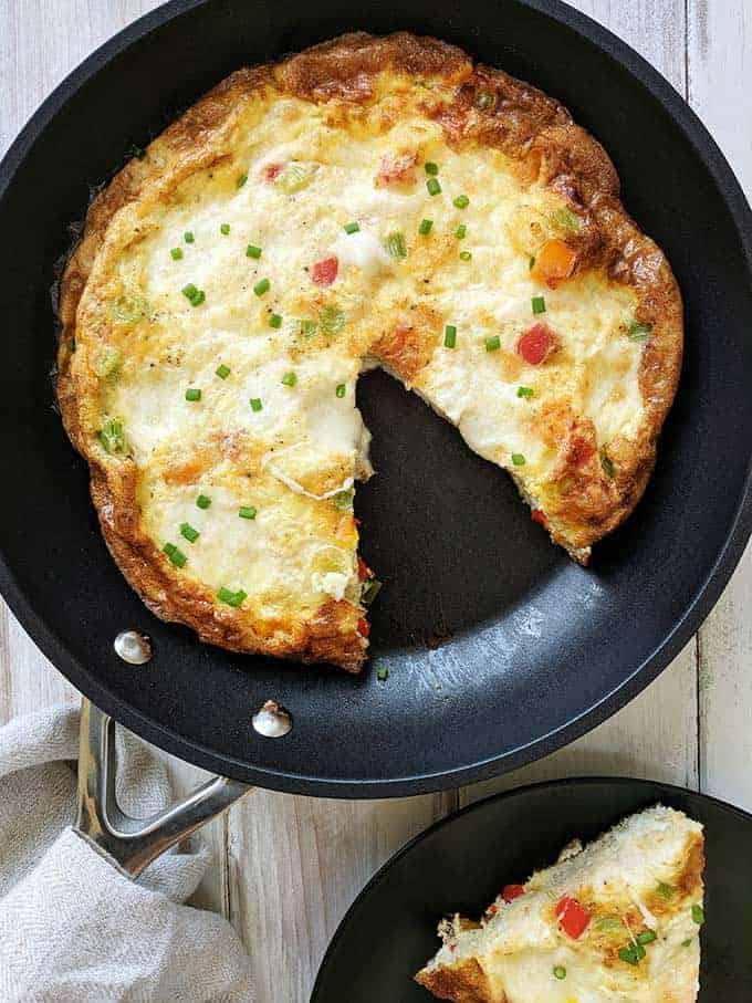 A skillet of sweet pepper frittata with mozzarella on a white table