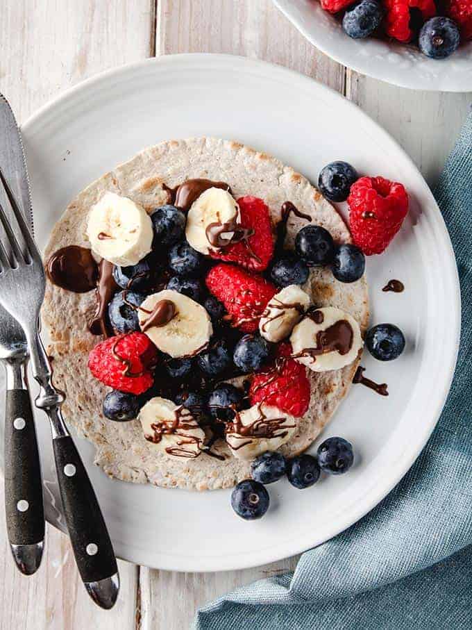 A taco with berries, banana and chocolate on a white plate