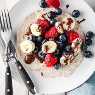 A berry breakfast taco on a white plate with black cutlery