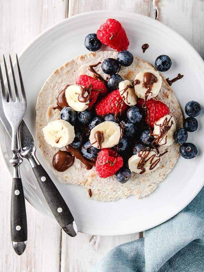 A berry breakfast taco on a white plate with black cutlery