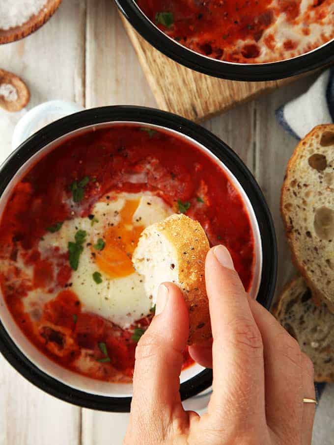 A dish of shakshuka with bread being dipped in it