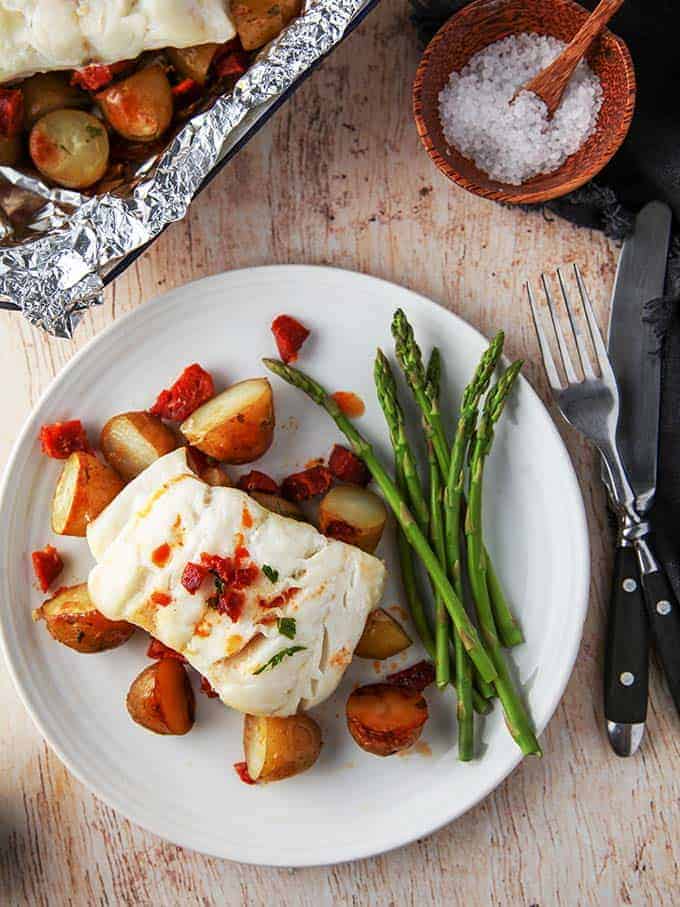 A plate of bake cod & chorizo with new potatoes on a wooden table